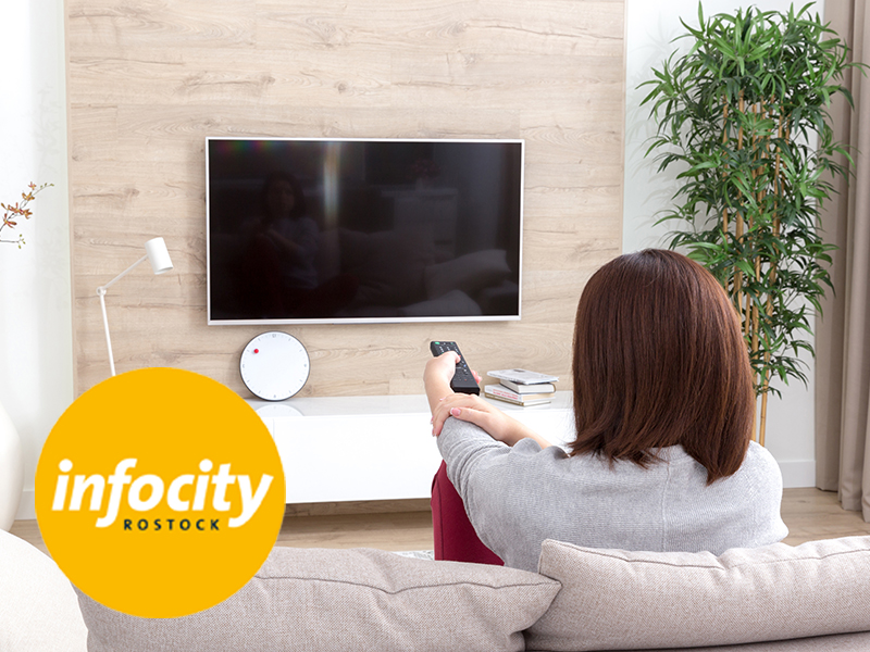 Frau im Wohnzimmer vor TV mit Fernbedienung in der Hand, Logo von Infocity